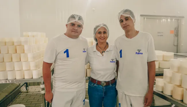 Equipe da queijaria diante das formas de queijo